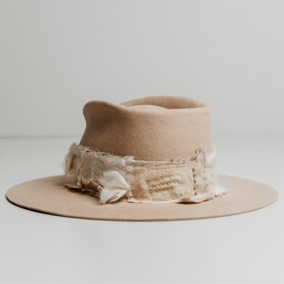 Back left angle of the Sabi Limited Edition Beige felt hat by PHYLLi Designs featuring the Wabi Sabi patch band with sashiko stitching and scattered matte gold bead accents.