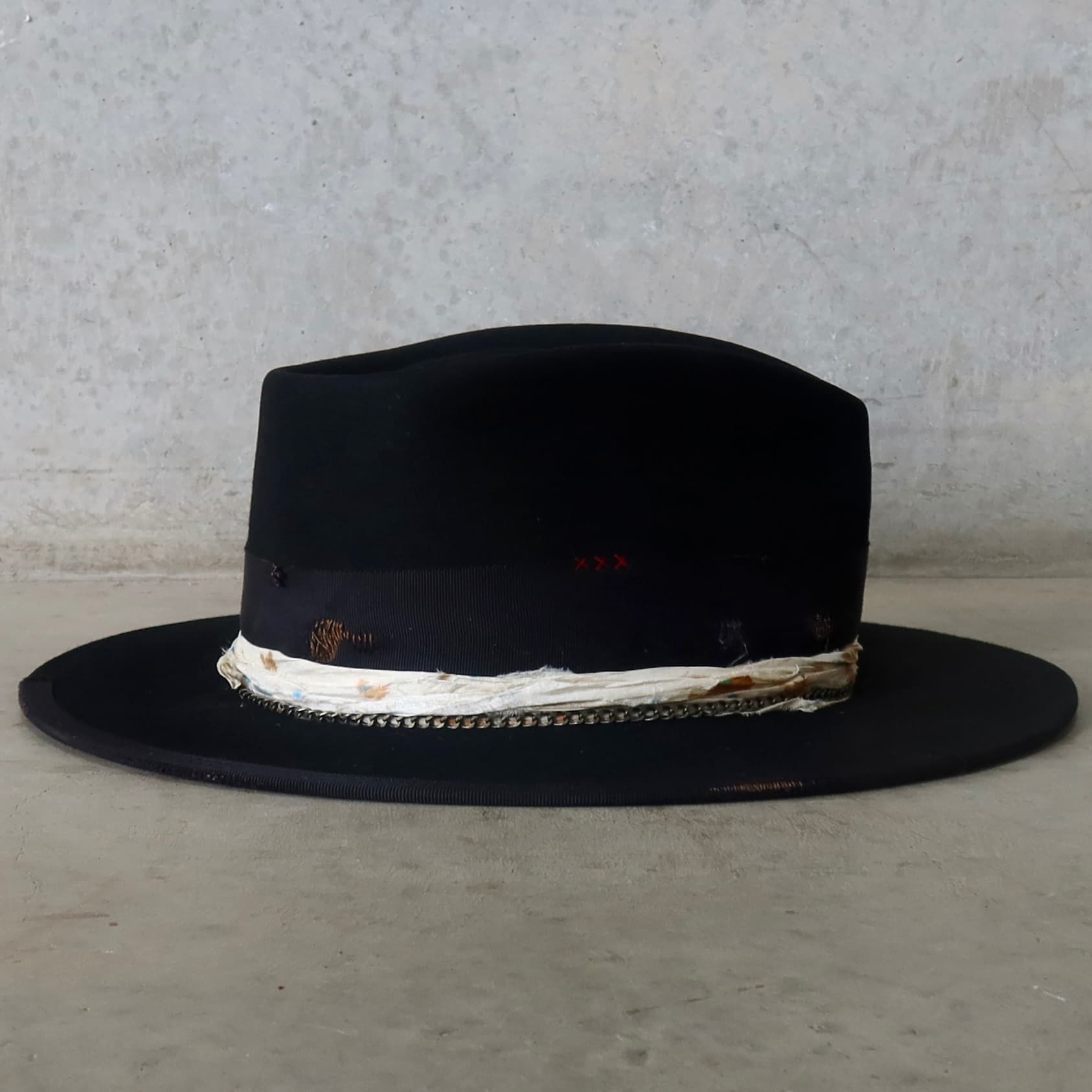 Right side view of the black felt hat Saint by PHYLLi Designs with burgundy hand-stitched crosses and bronze crown chain.