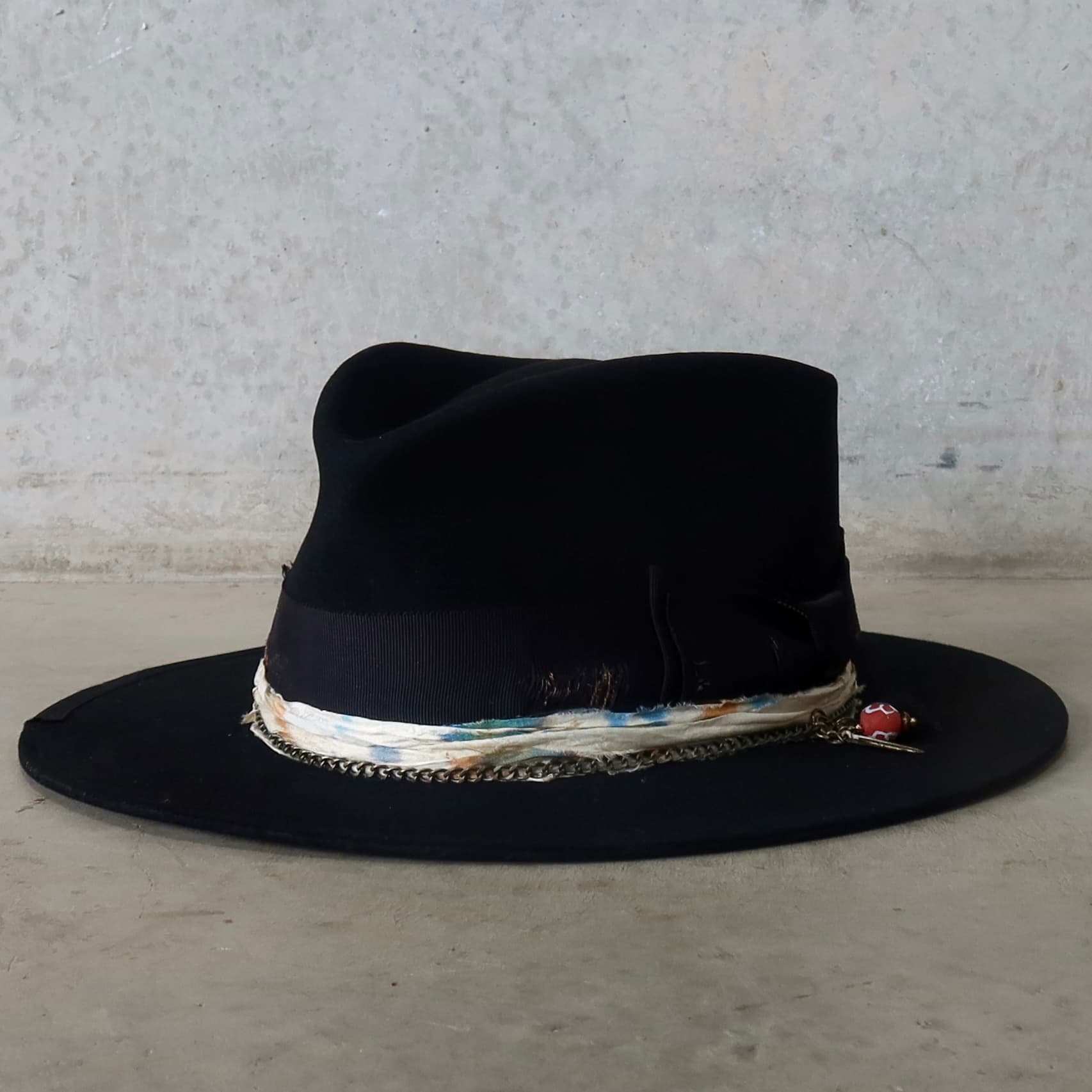 Front left angle of the black felt hat Saint by PHYLLi Designs with distressed grosgrain bow band, sari silk trim and bronze crown chain.