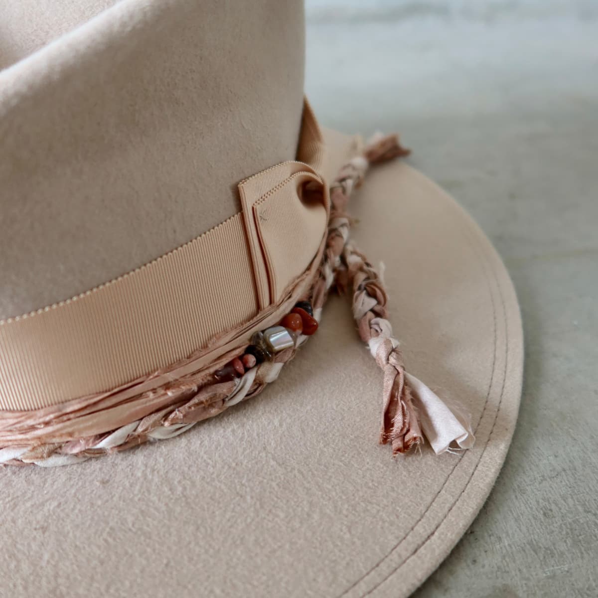 Close up detail of the Sandstone Limited Edition felt hat showing apricot Japanese grosgrain double bow band with plaited sari silk trimming in tonal colours.