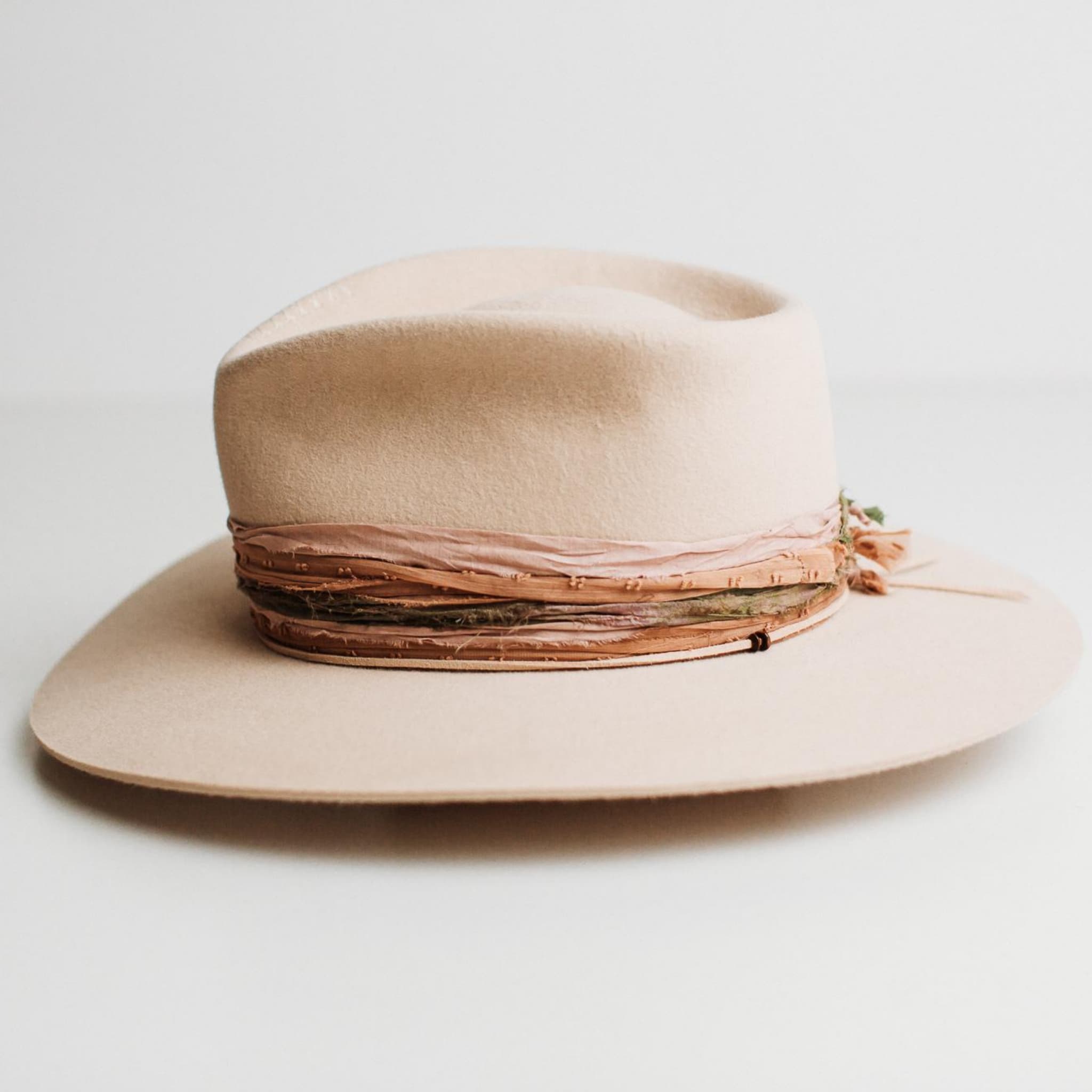 Left side view of Santa Fe Summer beige felt hat by PHYLLi Designs with plaster grosgrain band and nude suede string with wooden beads.