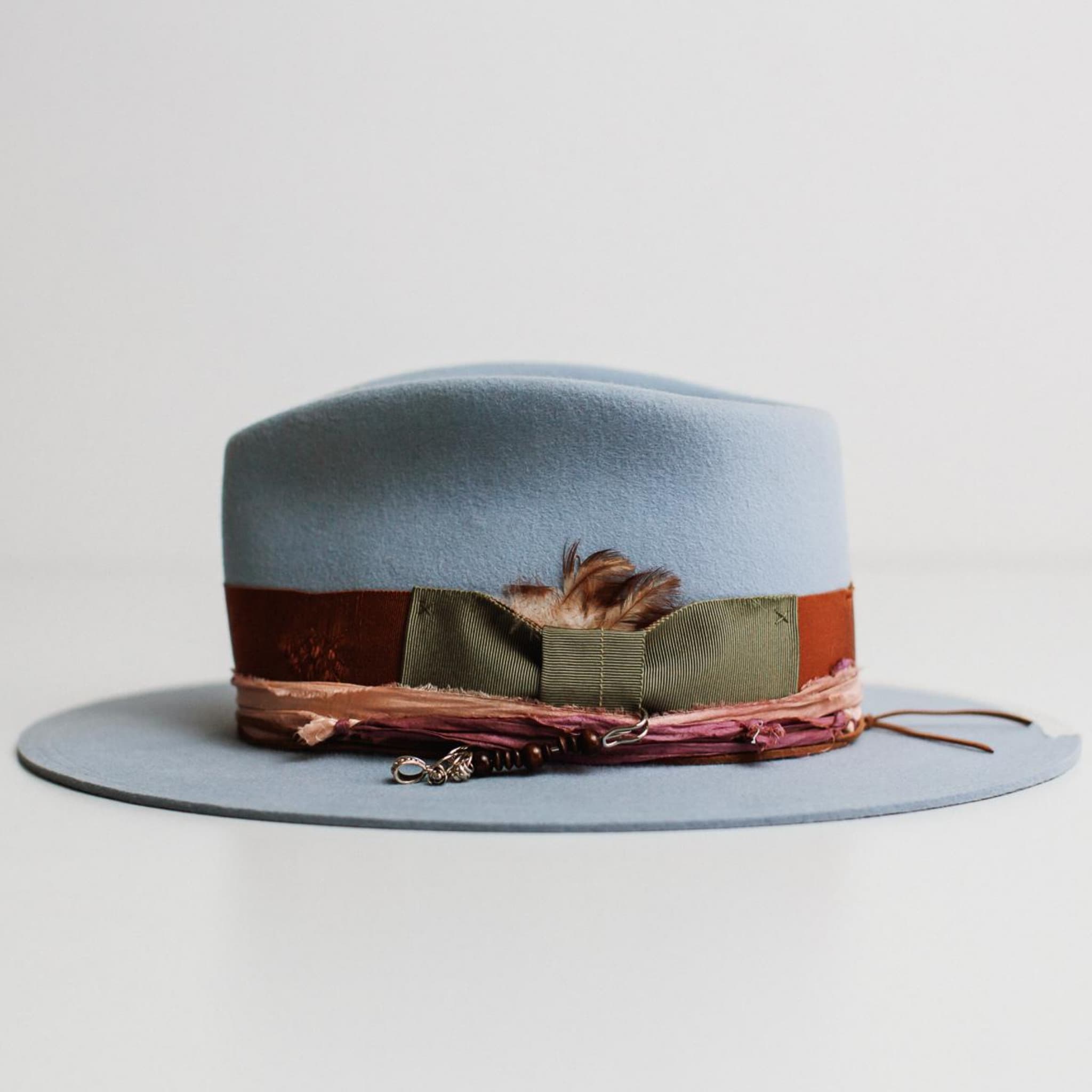 Left side view of Santa Monica crystal blue felt hat by PHYLLi Designs with rust band and silver hat pin detail.