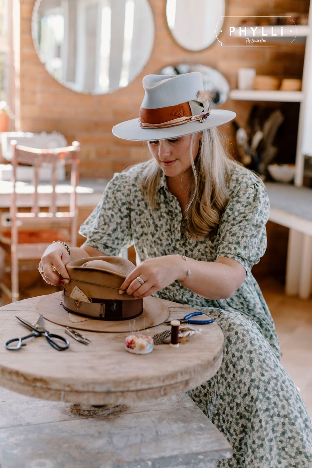 Laura Hall trimming a felt hat at the worktable in the PHYLLi Designs studio wearing the Santa Monica hat.