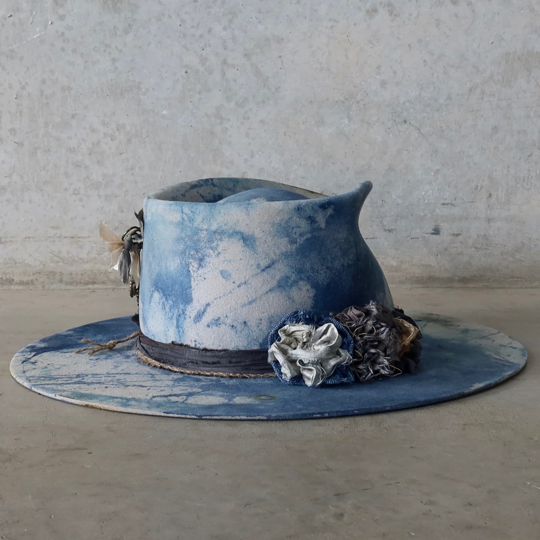 Back right angle of the dove grey indigo tie dye felt hat Shibori Limited Edition by PHYLLi Designs with three sari silk lapel blooms.