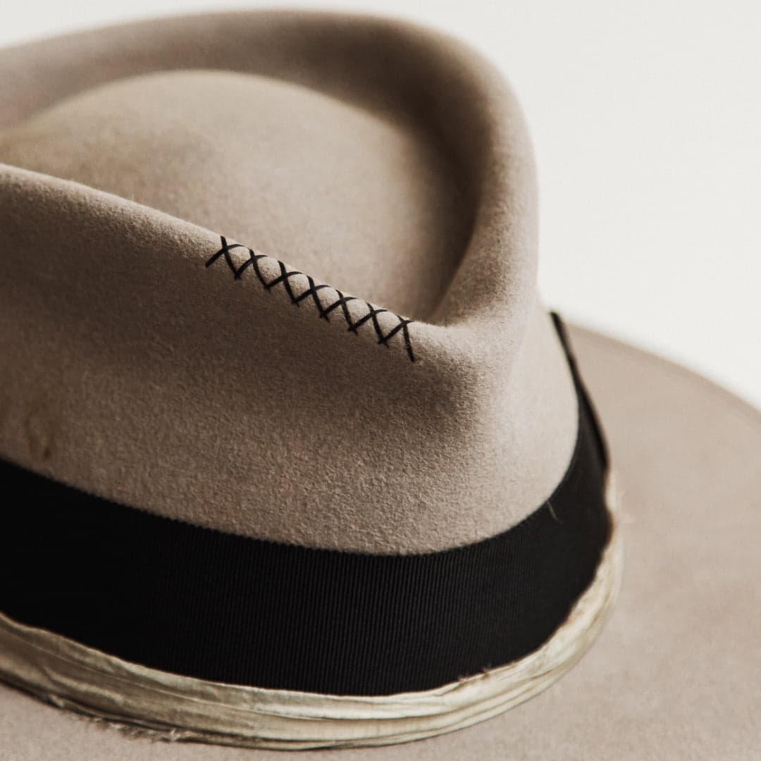 Close up detail of the Specter felt hat showing hand-stitched cross detailing in dark navy on the taupe crown.