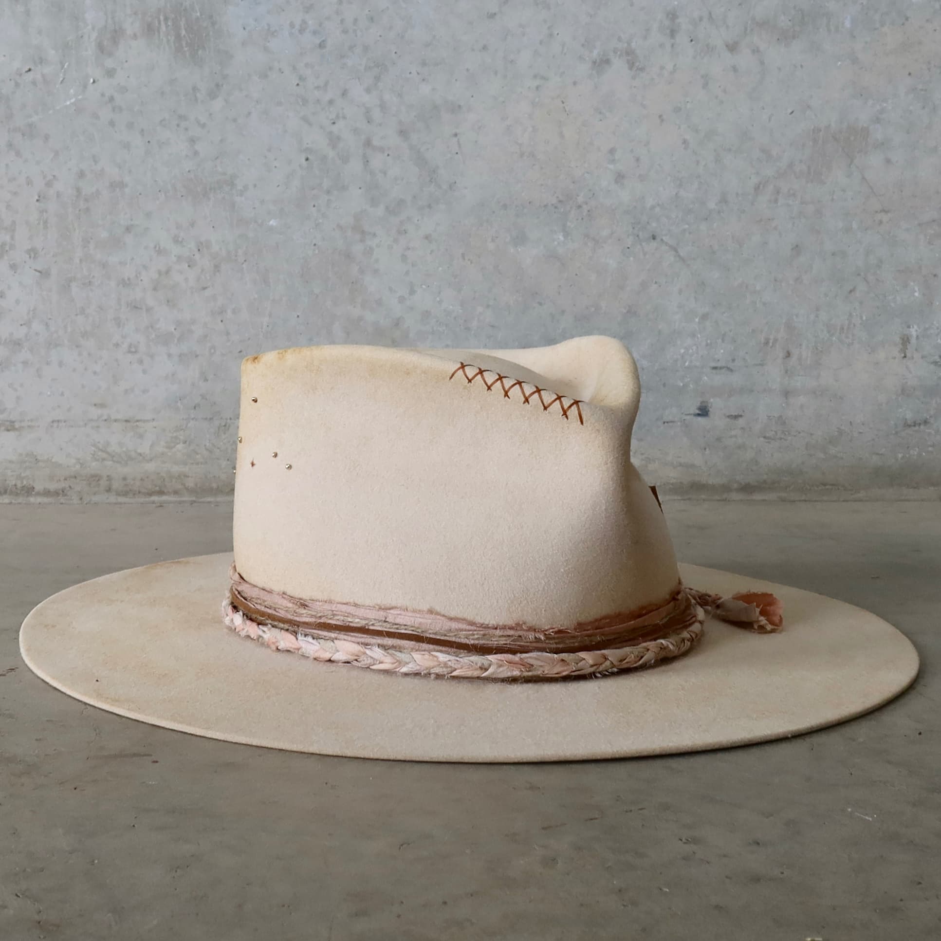 Front right angle of the beige distressed felt hat Starlight by PHYLLi Designs with copper cross stitching on the crown.