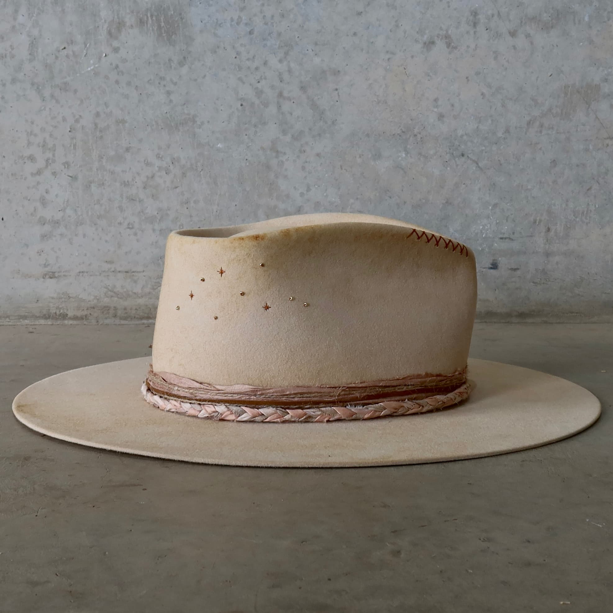 Right side view of the beige distressed felt hat Starlight by PHYLLi Designs with plaited sari silk trimming and copper twinkle star stitching with gold glass bead details.