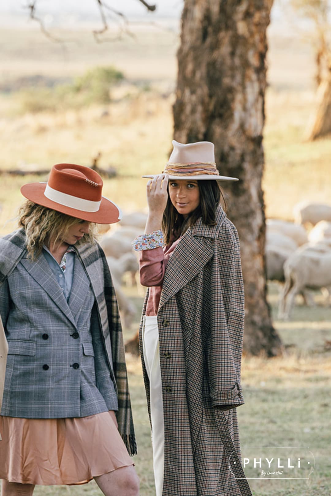 oman wearing the Sunset sand felt hat by PHYLLi Designs with a checked coat and blush shirt, standing outdoors beside another woman in a pumpkin felt hat.