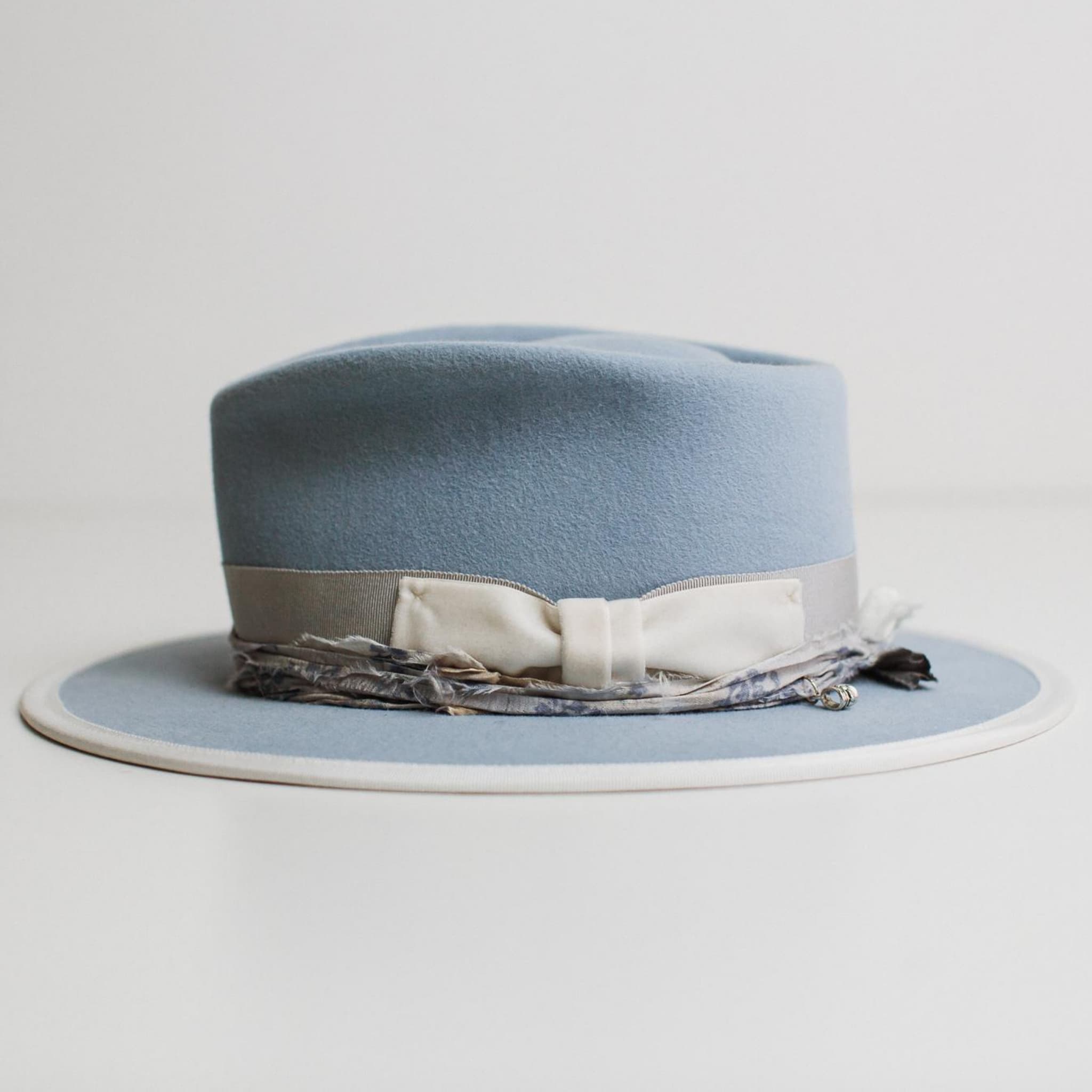 Left side view of The Arrow crystal blue felt hat by PHYLLi Designs with ivory grosgrain brim trim and dusty blue sari silk trimming.