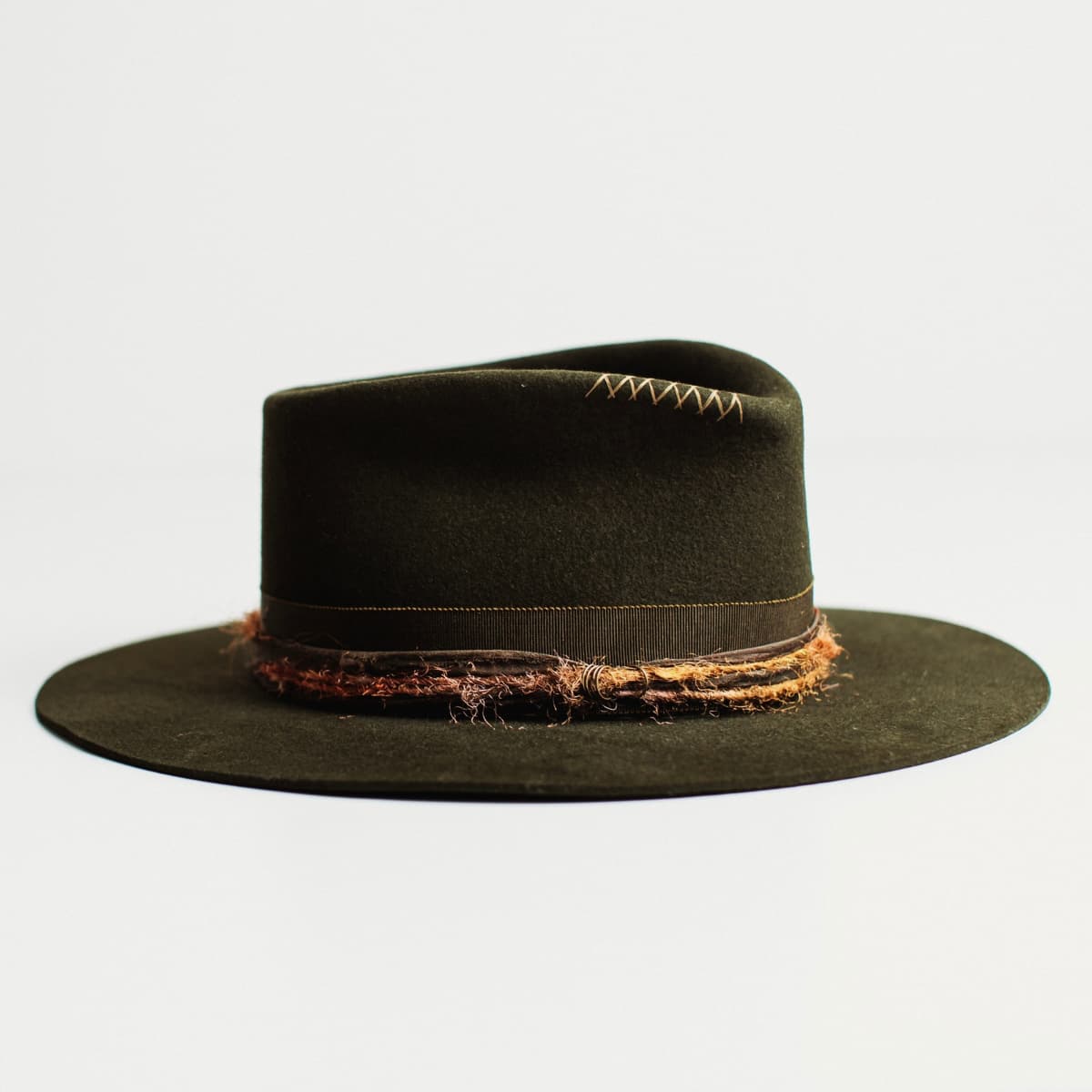 Front right angled view of dark olive felt hat with distressed layered band by PHYLLi Designs on a light grey background.