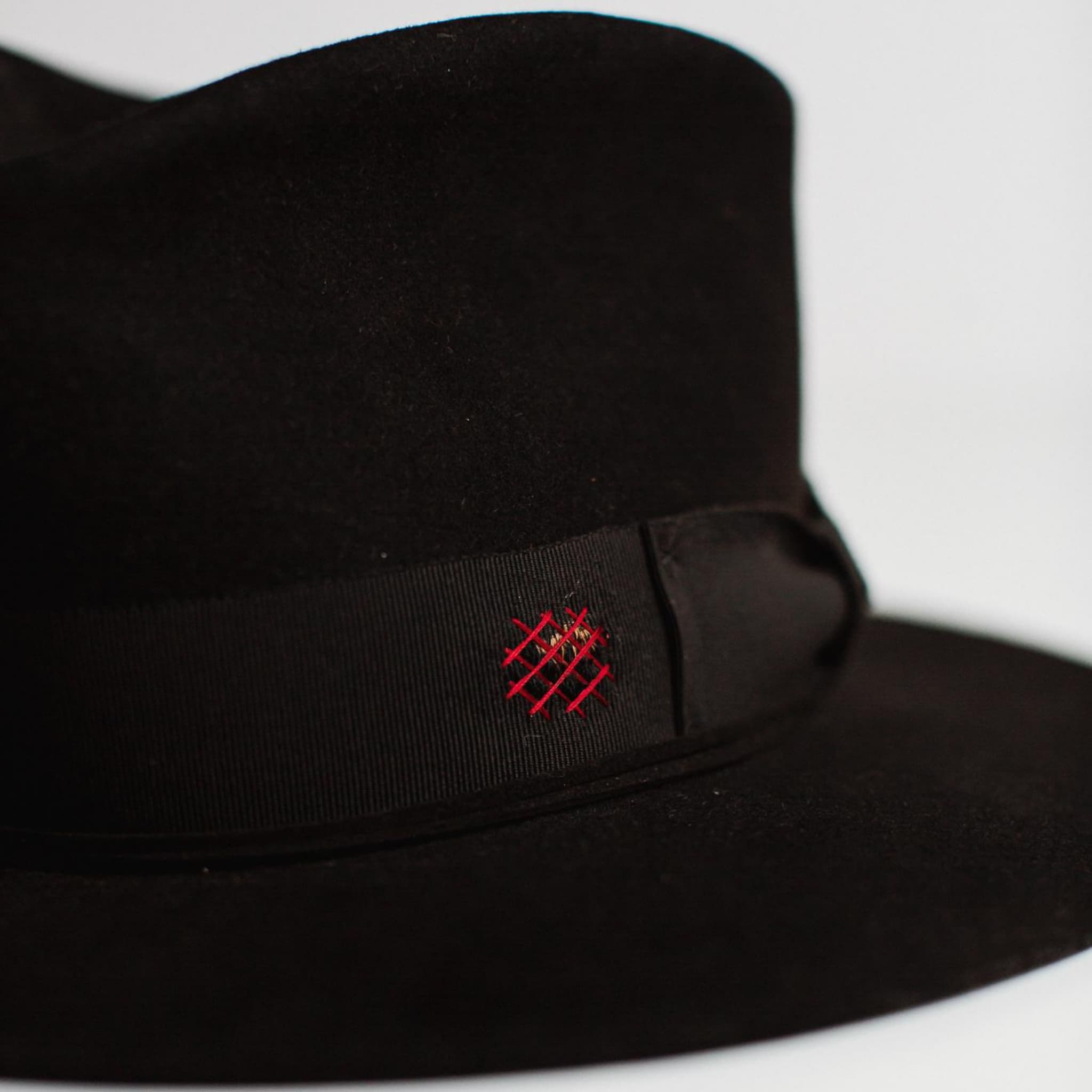 Close up detail of The Betty black felt hat by PHYLLi Designs showing burgundy distressed patches, black grosgrain band and handcrafted stitching.