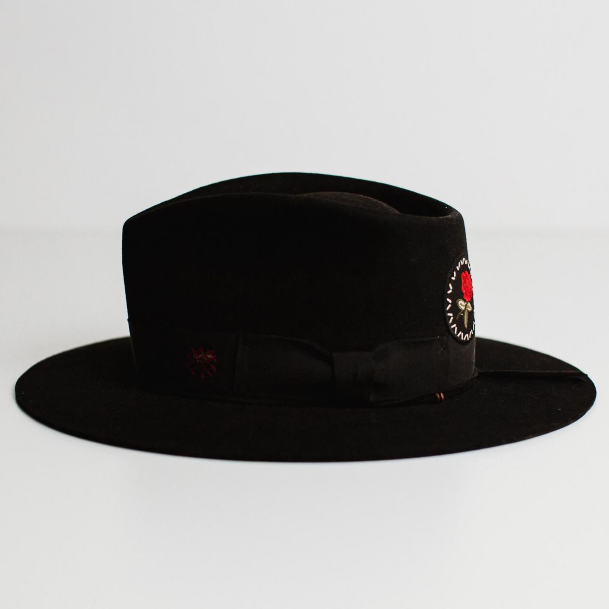 Left side view of The Betty black felt hat by PHYLLi Designs with black grosgrain band, burgundy distressed patches and black suede string with wooden beading.