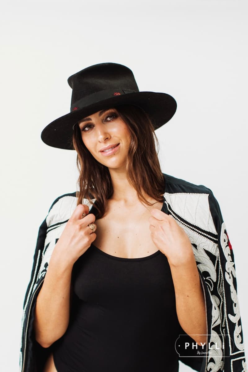 Model wearing The Betty black felt hat by PHYLLi Designs with black grosgrain band and burgundy patch detailing.