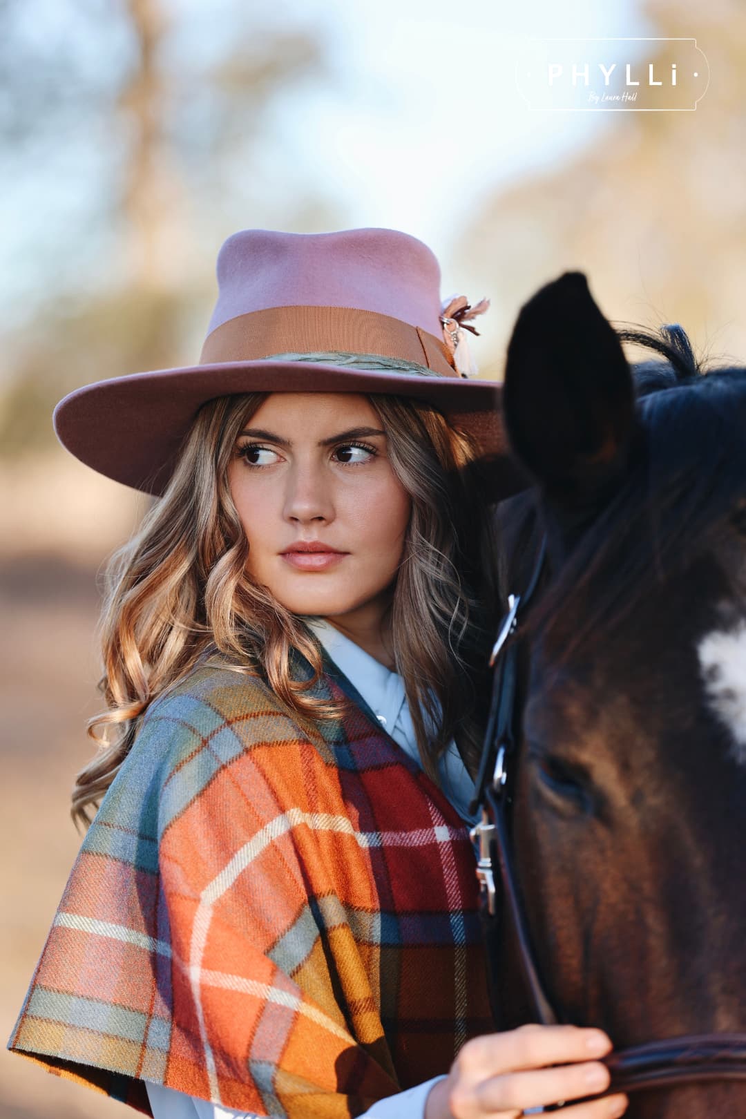 Woman wearing The Blush felt hat by PHYLLi Designs beside horse in golden hour countryside.