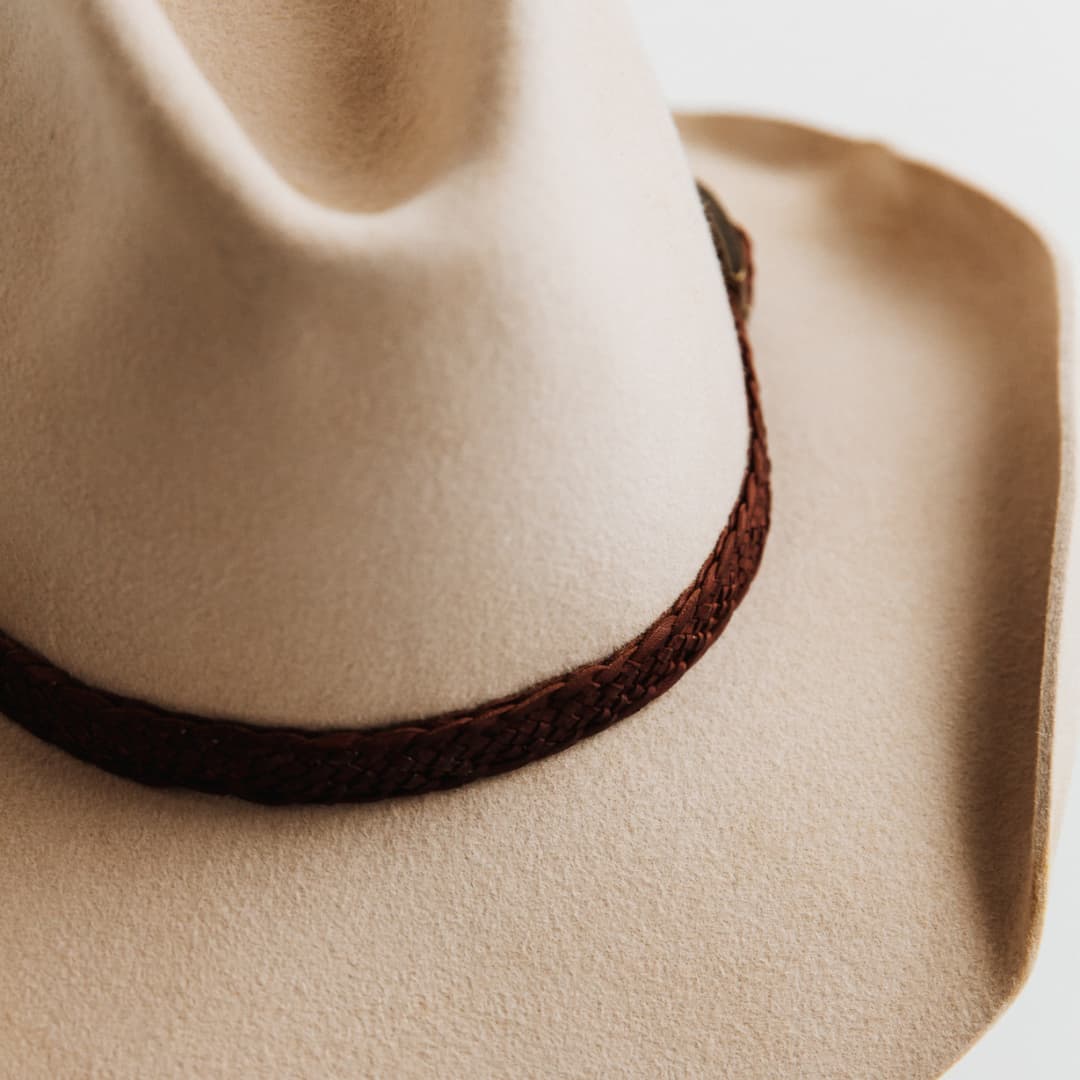 Close up detail of 12 strand plaited leather hat band in Chocolate featuring bronze buckle on The Contractor premium felt hat in Beige.