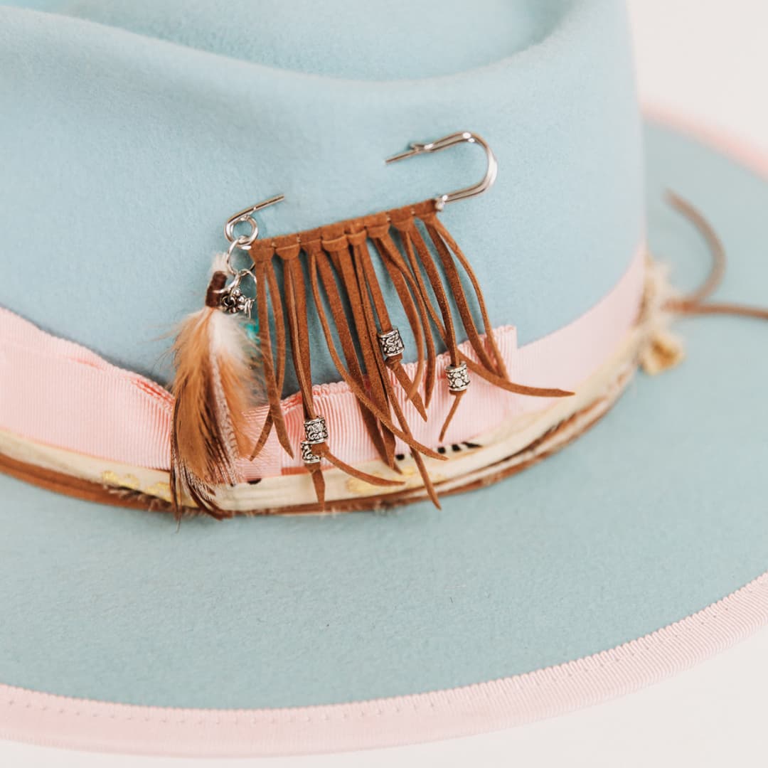 Close up detail of The Cyan felt hat by PHYLLi Designs featuring silver chunky hat pin with suede fringing, feathers, silver and turquoise beading.