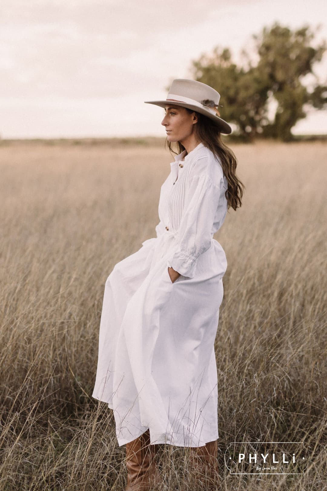 Side profile of woman wearing The Dartbrook beige felt hat by PHYLLi Designs in open countryside.