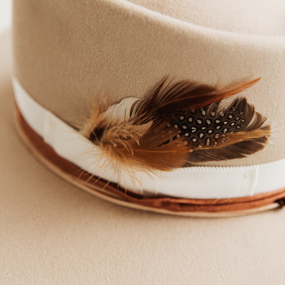 Close up of feather bunch, ivory grosgrain band and rust sari silk trimming on The Dartbrook felt hat by PHYLLi Designs.