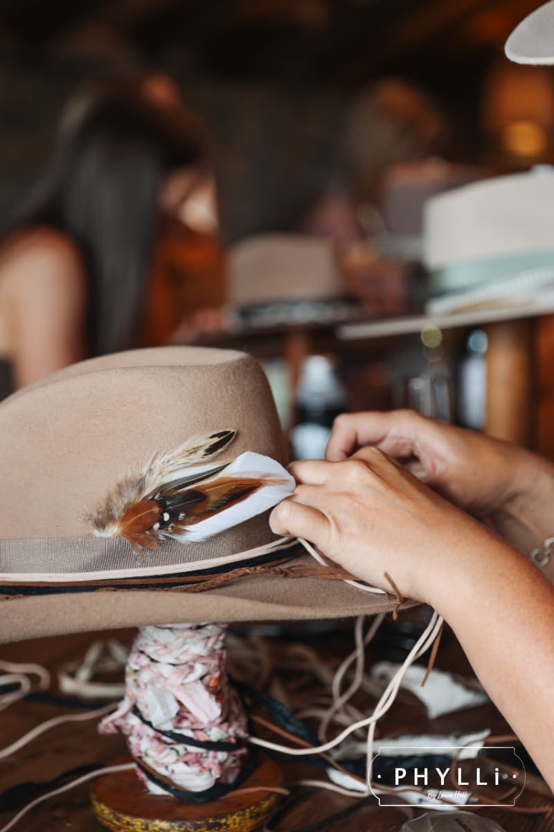 Guest attaching feathers and trims to personalise a felt hat at a PHYLLi hat party event.