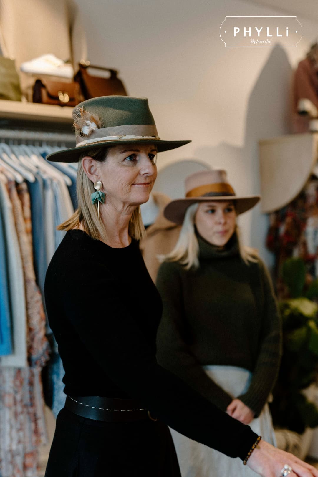 Woman wearing The Lotus Military felt hat by PHYLLi Designs standing in a boutique with clothing racks behind.
