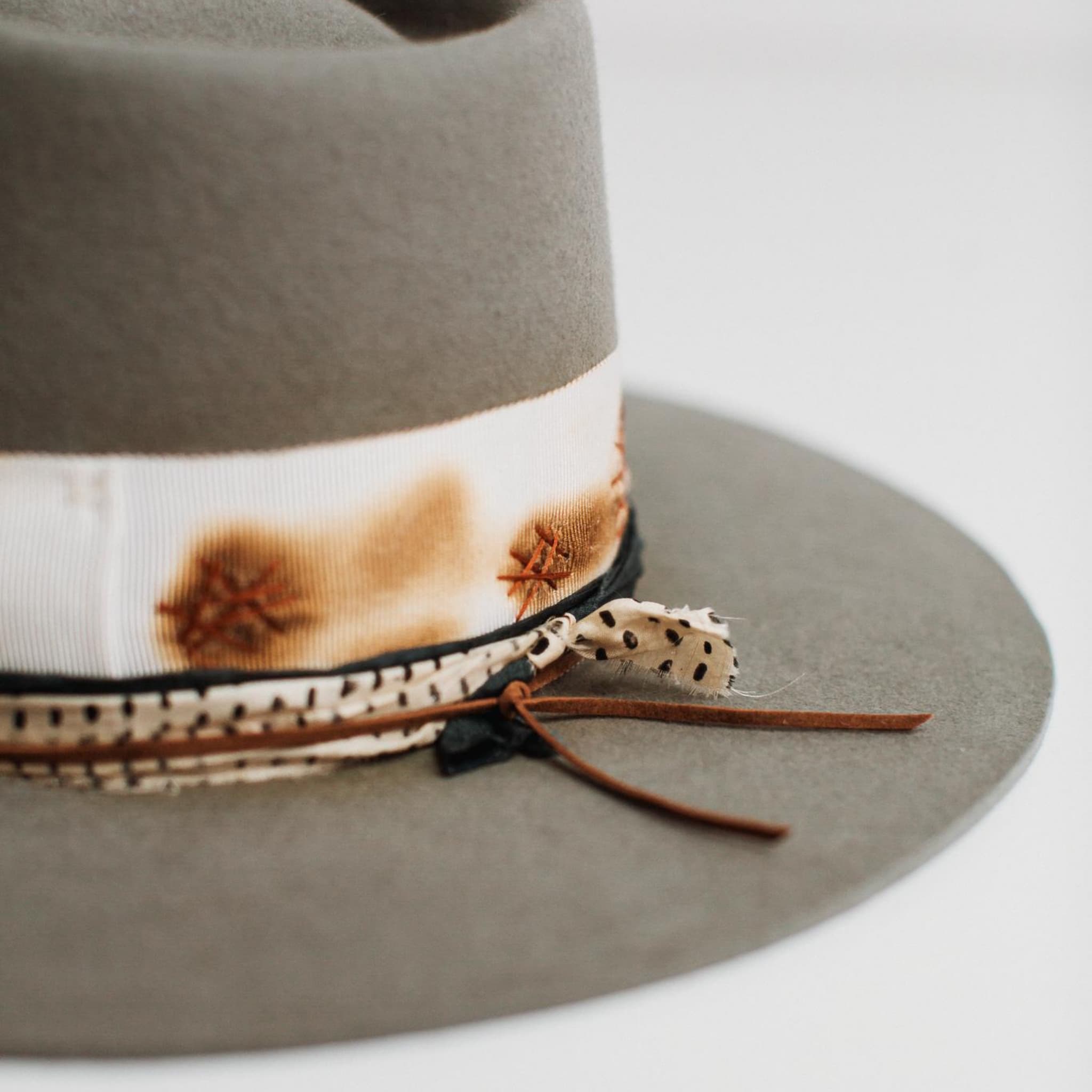 Close up detail of The Paver taupe felt hat trim with ivory grosgrain band, rust darning and sari silk trimming.
