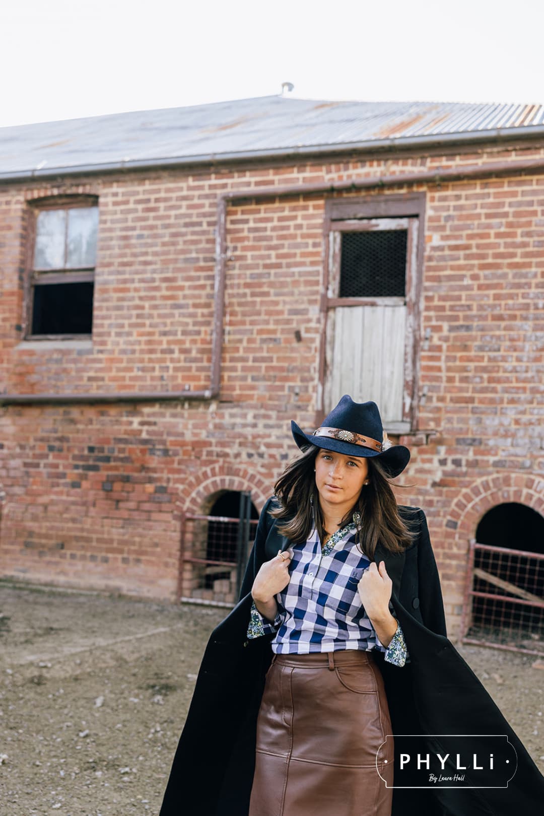 Model wearing The PHYLLi dark navy felt hat by PHYLLi Designs with leather tie back band inside a rustic timber barn.
