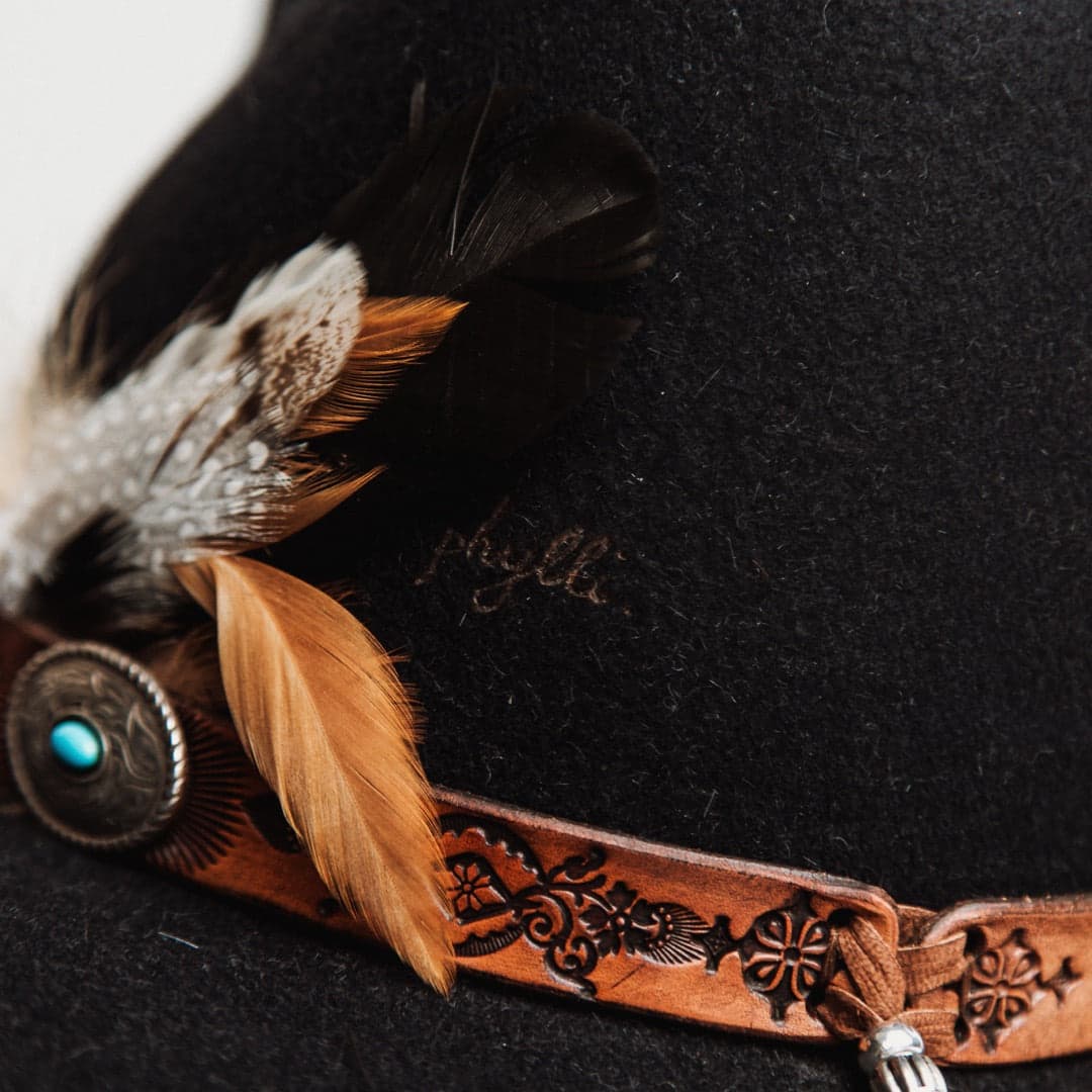 Close up detail of The PHYLLi felt hat showing fallen feather bunch and engraved leather hat band with turquoise concho.
