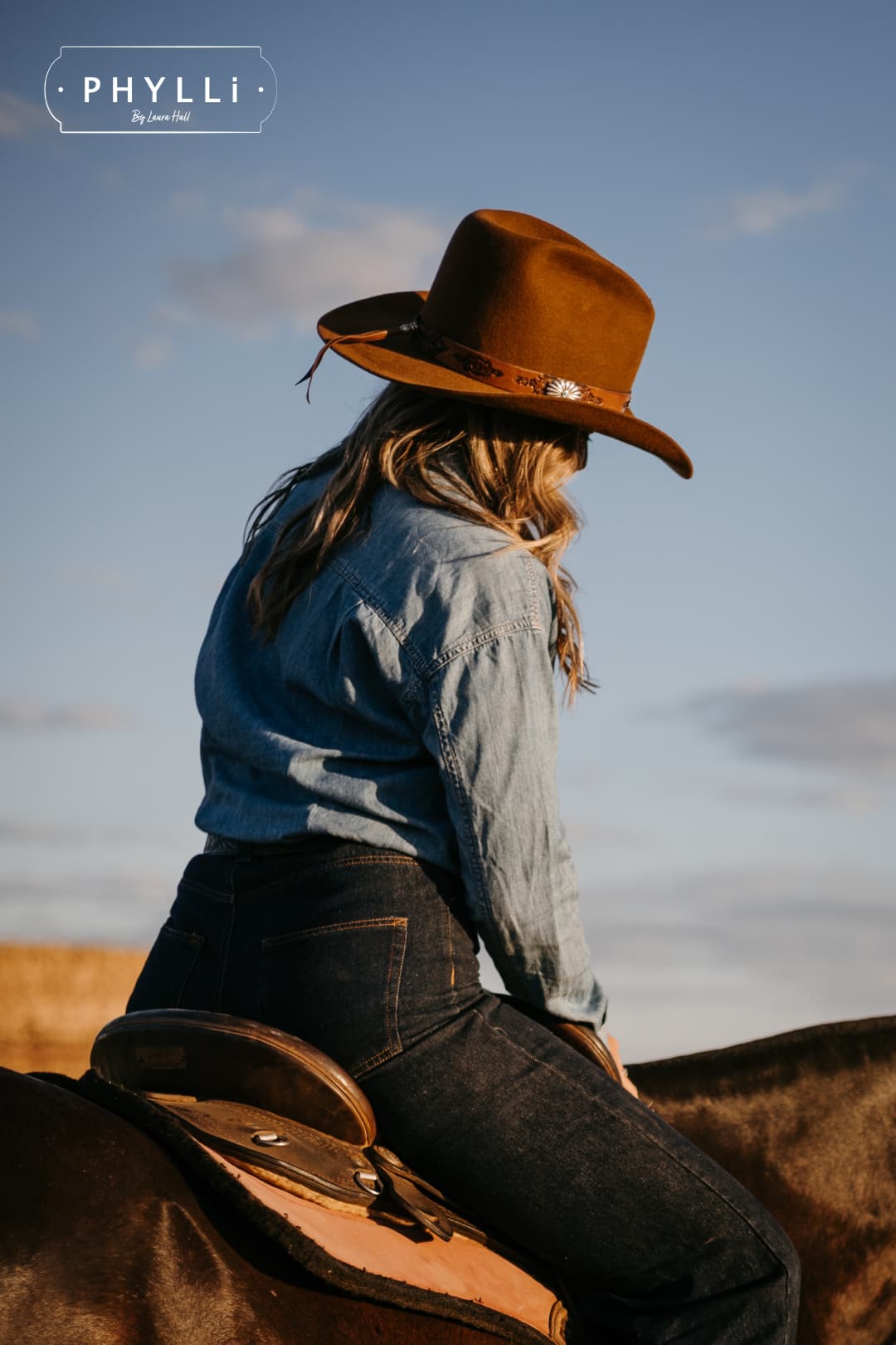 Cowgirl wearing the Caramel cowboy hat The PHYLLi Caramel by PHYLLi Designs with Buffalo Girl Western floral tie back hat band while riding horseback.