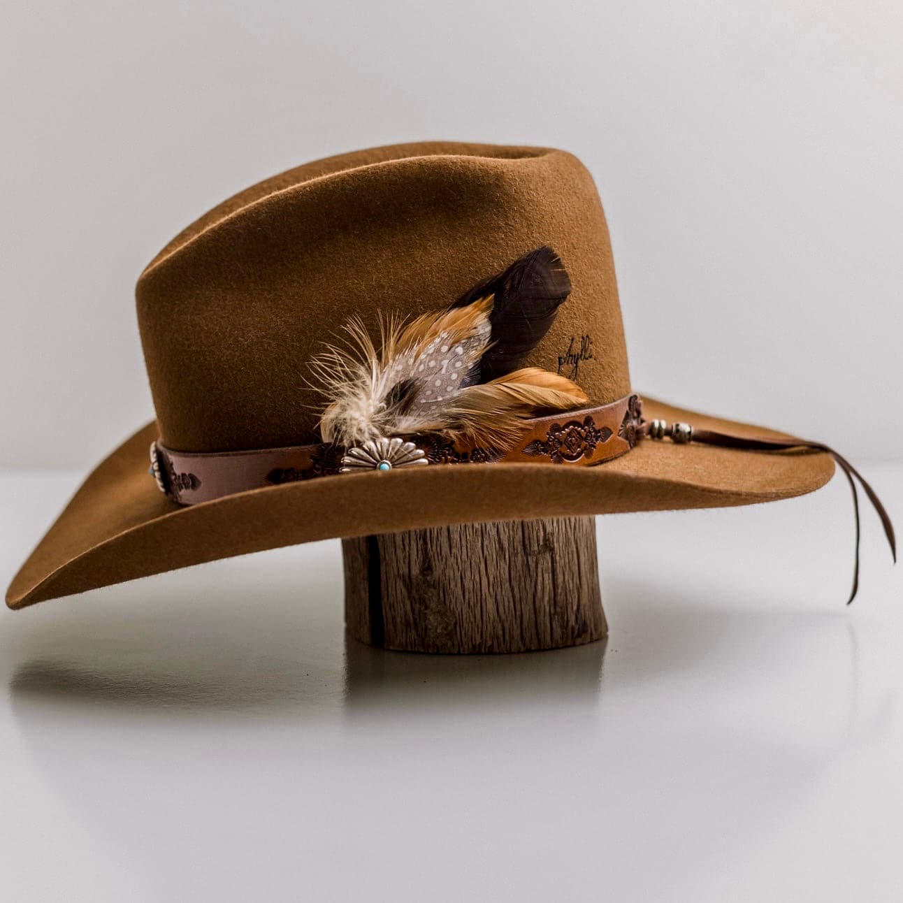 Left side view of the Caramel cowboy hat The PHYLLi Caramel by PHYLLi Designs with Buffalo Girl Western floral tie back hat band and fallen feather bunch.