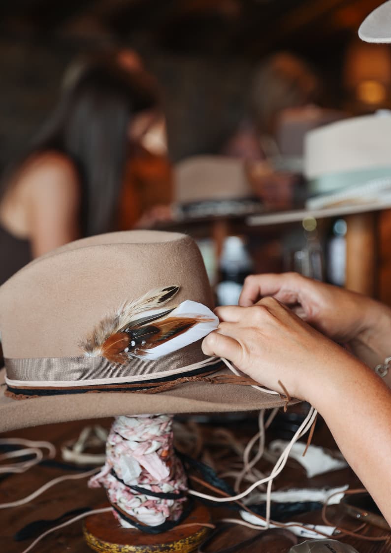 Customising a camel felt hat with feathers and trim at a PHYLLi Hat Bar experience by PHYLLi Designs.