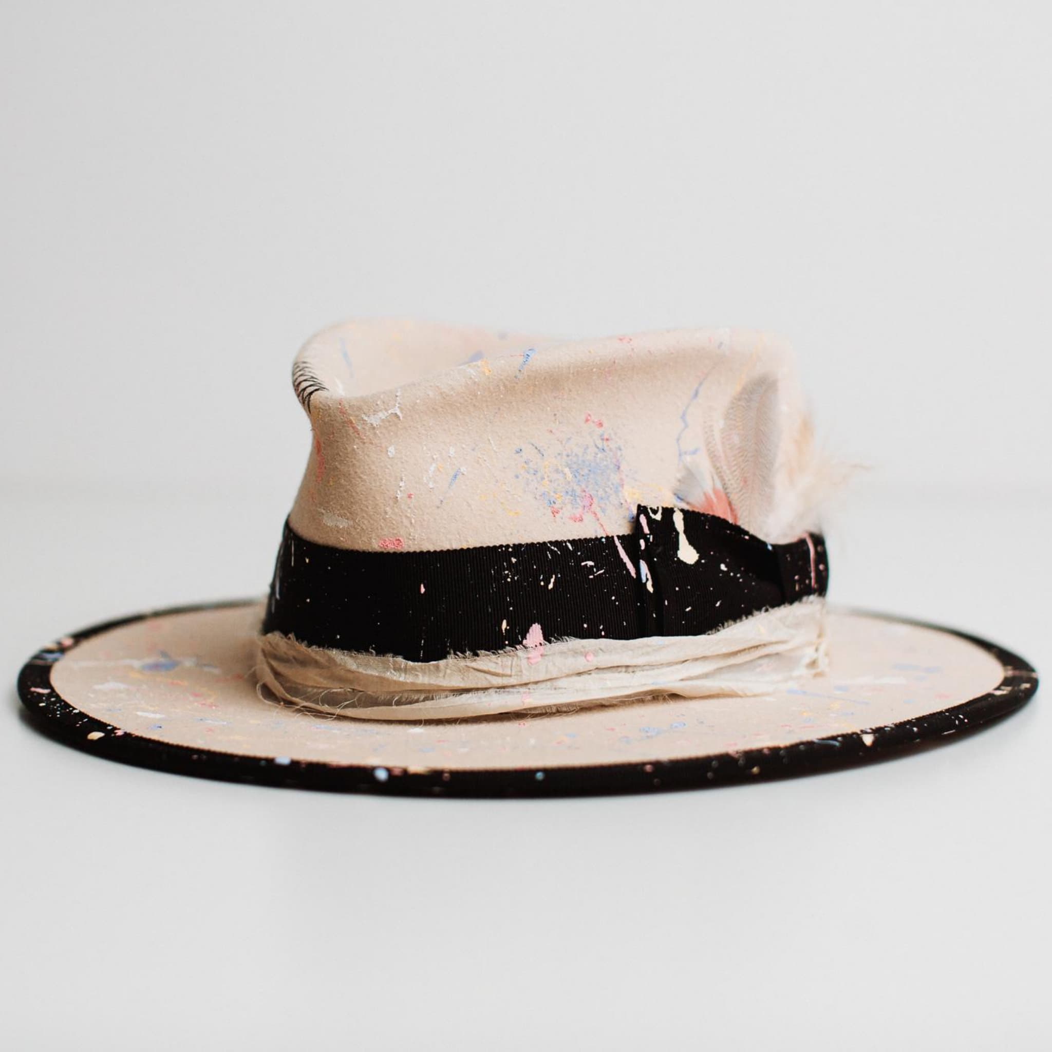Front left angle of Pollock beige felt hat by PHYLLi Designs featuring paint splatter finish and black grosgrain band.