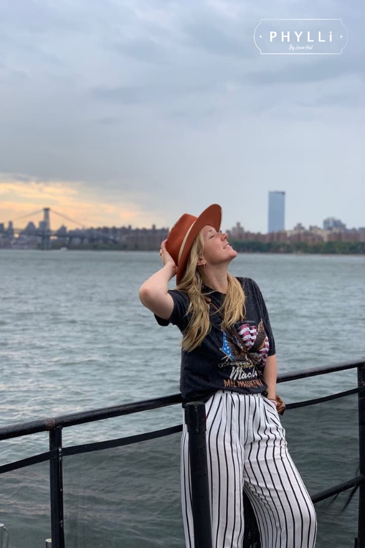 Woman wearing the spiced pumpkin Producer felt hat with a city skyline and waterfront backdrop.