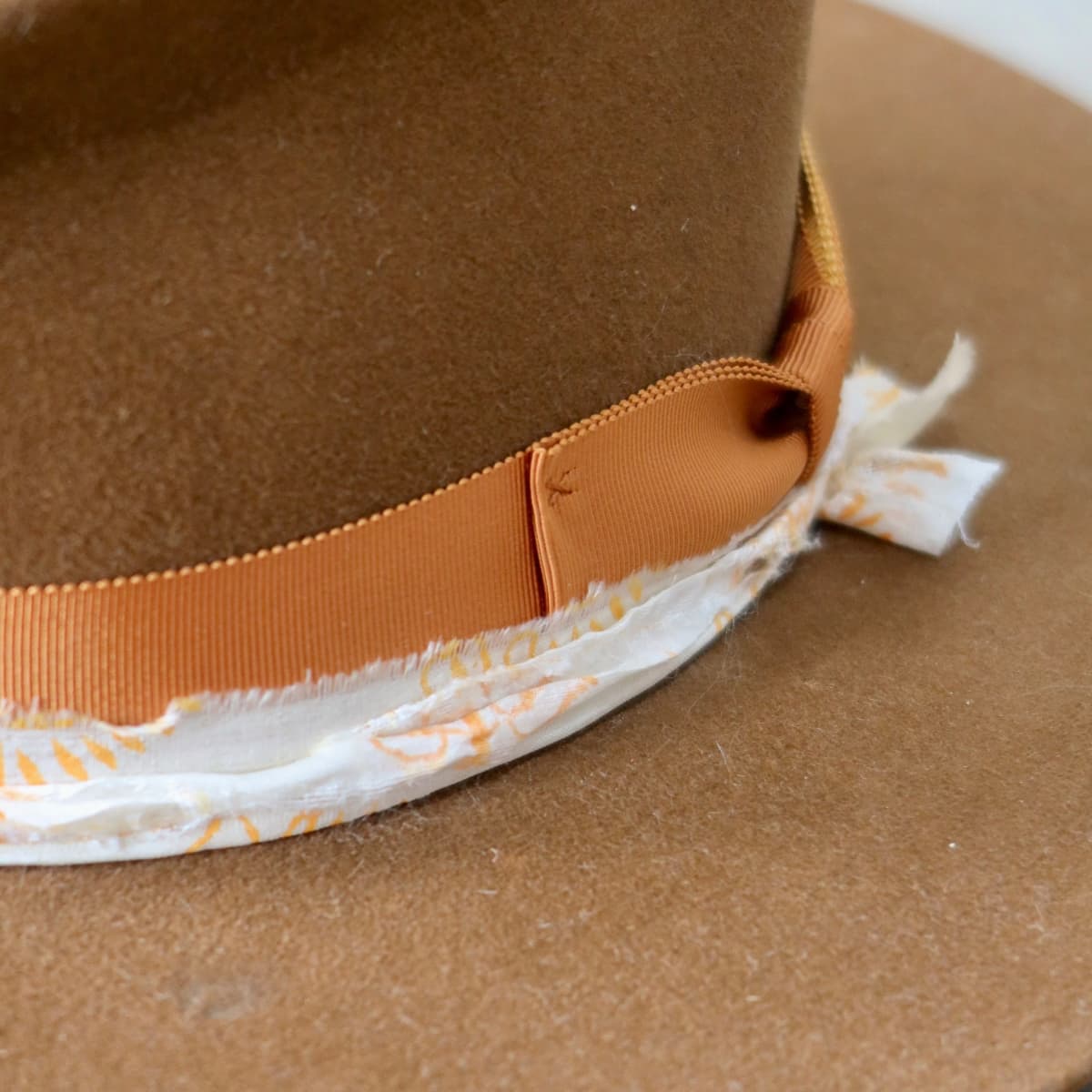 Close-up of grosgrain band and patterned silk trim layered around caramel felt hat by PHYLLi Designs.