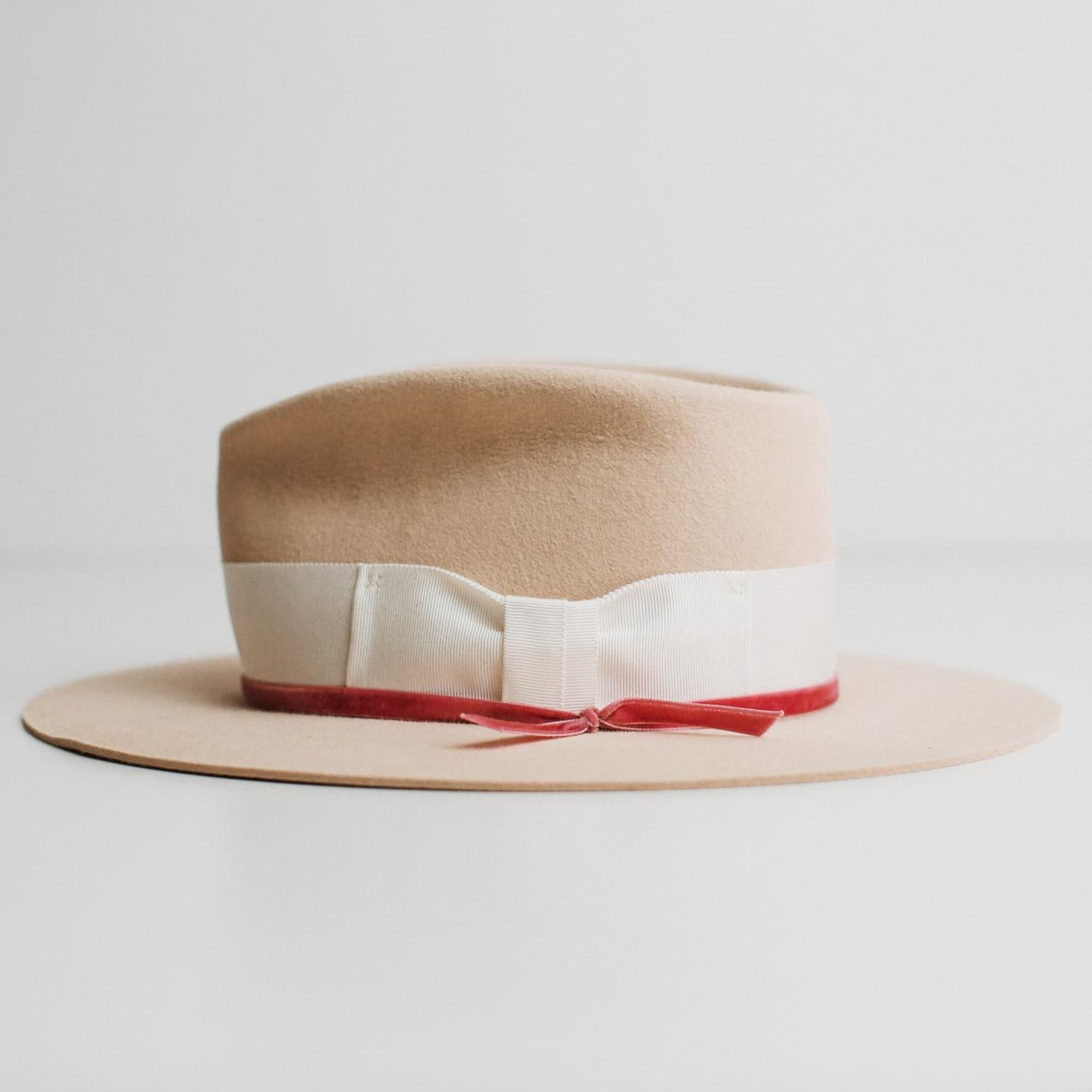Side view of beige felt hat with ivory band and pink velvet ribbon by PHYLLi Designs on a light grey background.