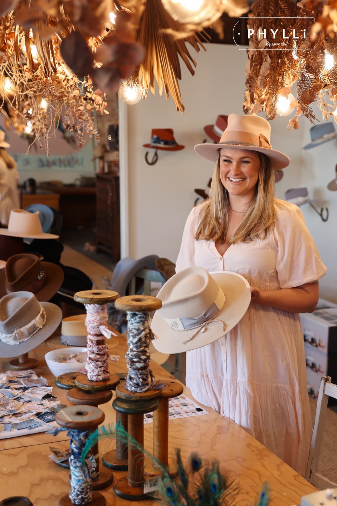 PHYLLi founder Laura Hall wearing the Tourmaline Baby Pink felt hat by PHYLLi Designs with rose quartz hat necklace while holding a hat in the PHYLLi workshop.