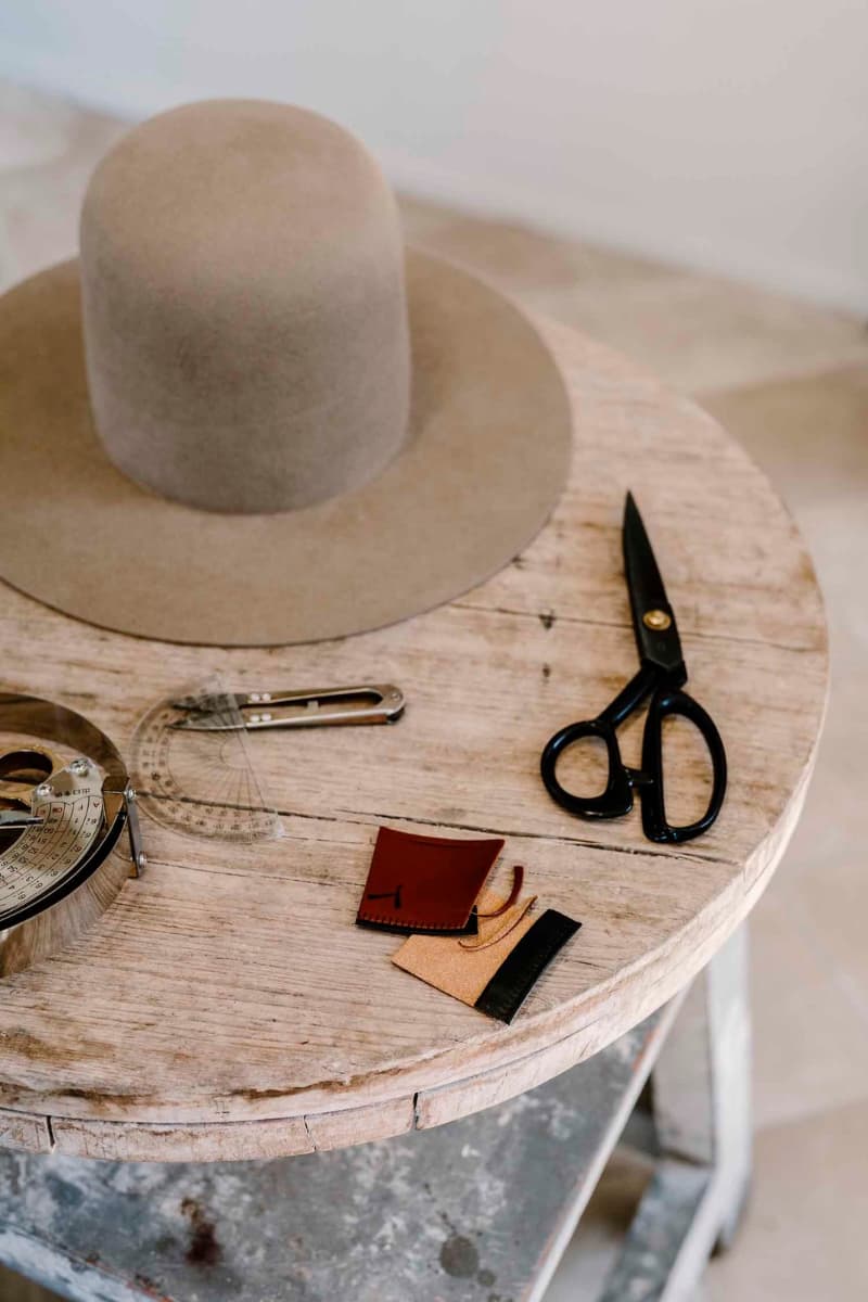 Felt hat base, scissors and measuring tools arranged on wooden workbench in the PHYLLi hat studio.