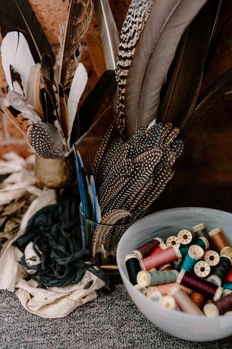 Assorted feather hat trimmings and thread spools arranged on studio table in the PHYLLi hat studio.