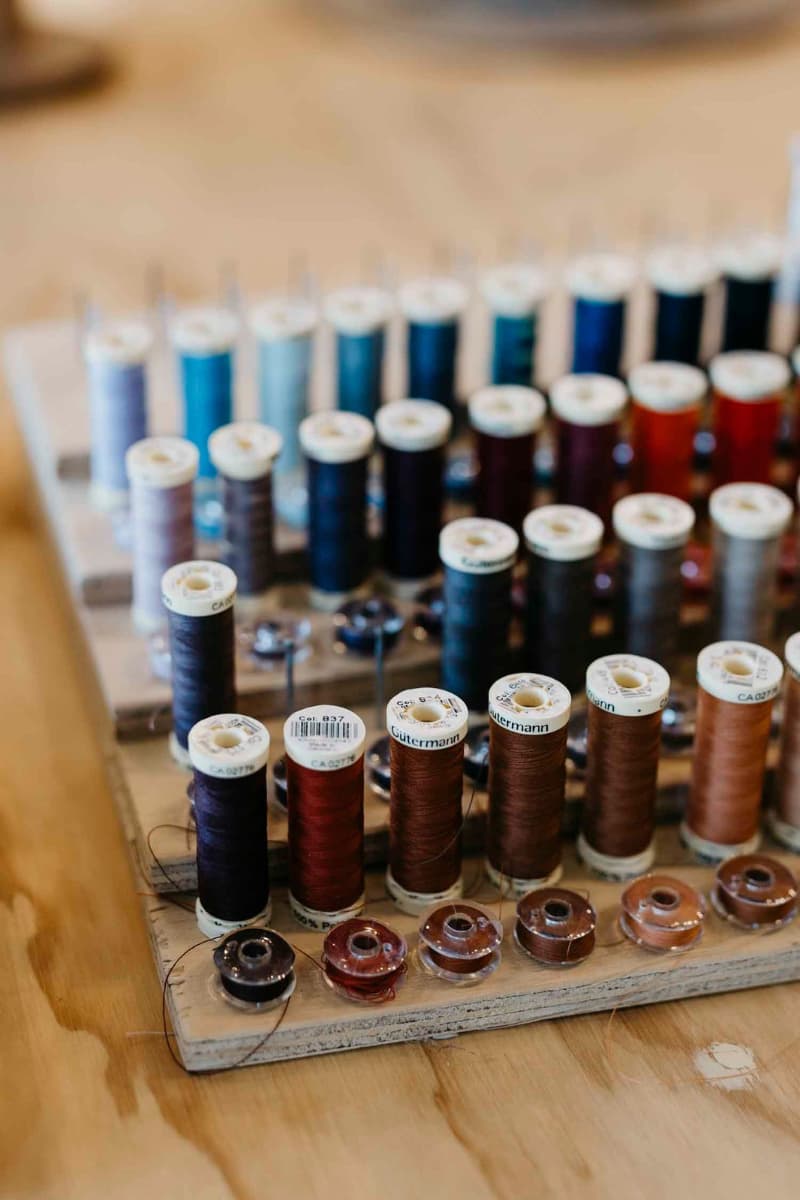Rows of sewing thread spools and bobbins organised on wooden stand in the PHYLLi hat studio.