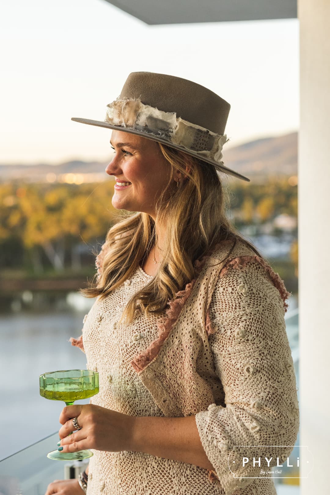 Laura Hall, founder of PHYLLi Designs, wearing the Wabi Limited Edition Sahara felt hat with sashiko stitched Wabi Sabi patch band in a sunset balcony setting.