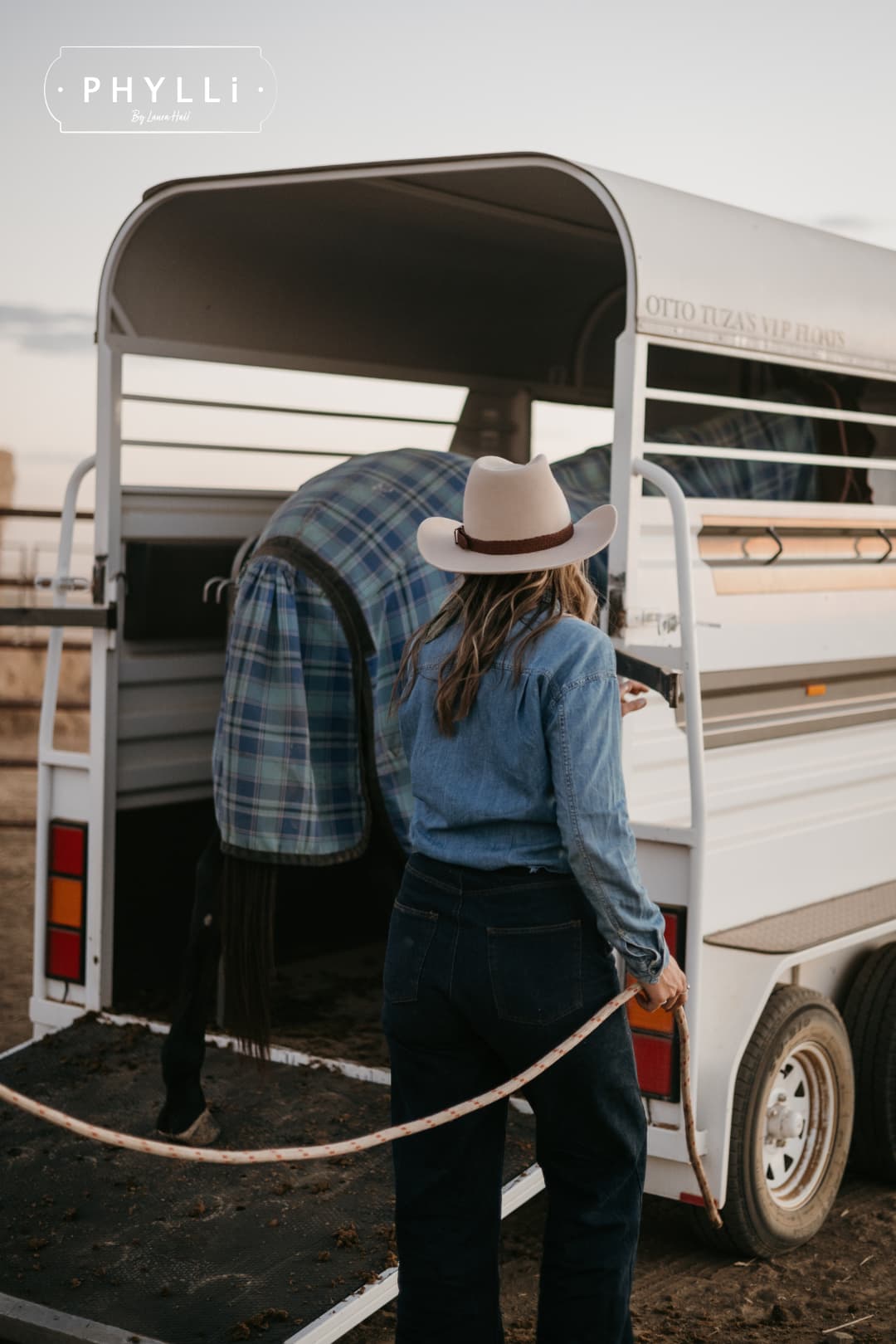Model wearing the beige cowboy hat Wheeler Beige by PHYLLi Designs with chocolate leather hat band while loading horses into a float.