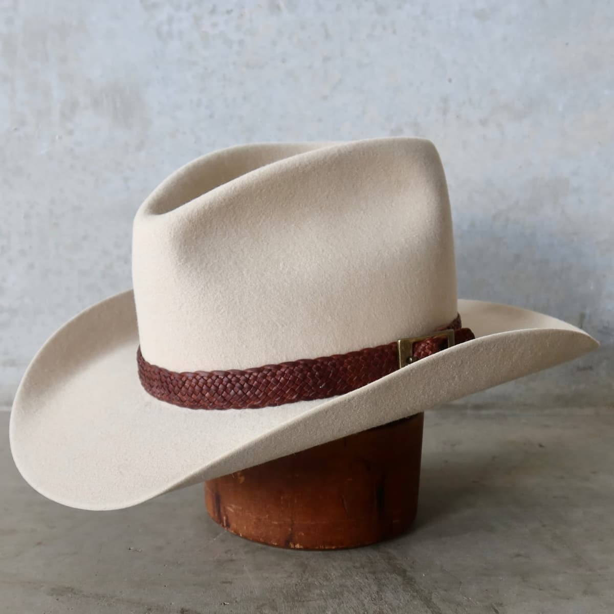 Front left angle of the beige cowboy hat Wheeler Beige by PHYLLi Designs with 12 strand chocolate leather hat band featuring bronze buckle.