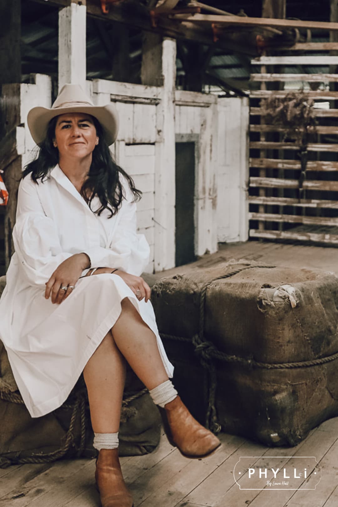 Woman wearing the Wrapped Wheeler beige felt hat by PHYLLi Designs with sari silk wrapped band in a rustic shearing shed.