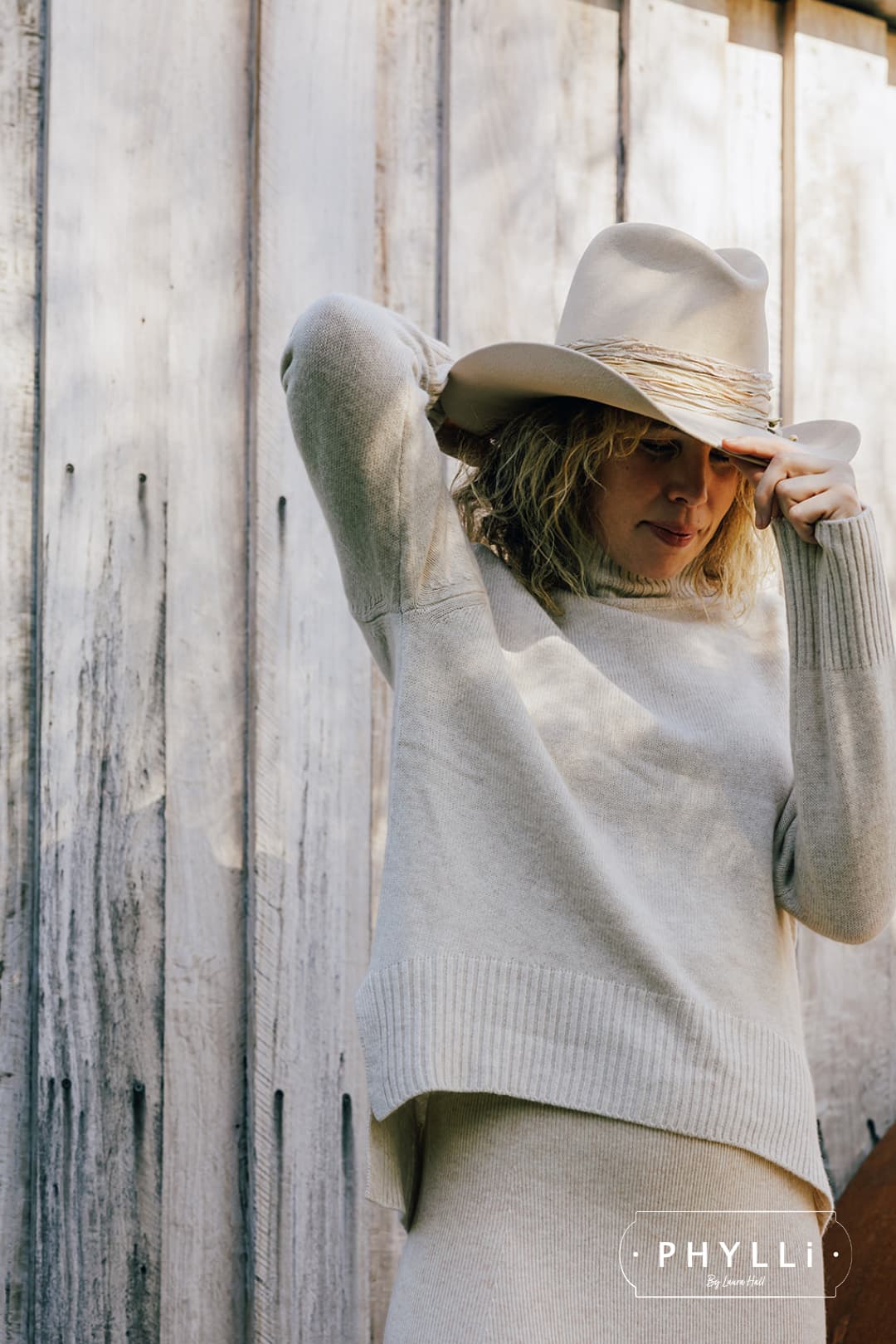 Woman wearing the Wrapped Wheeler beige felt hat by PHYLLi Designs with sari silk wrapped band in front of a weathered timber wall.