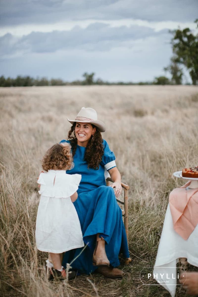 Woman wearing the Wrapped Wheeler beige felt hat by PHYLLi Designs with dusty pink sari silk wrapped band in a rural paddock.