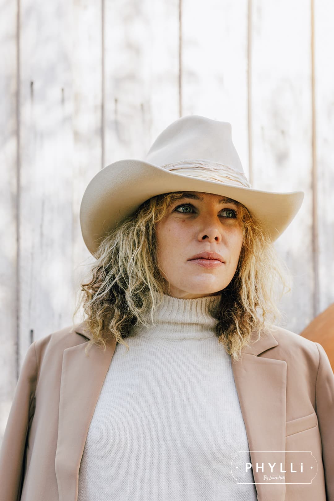 Woman wearing the Wrapped Wheeler beige felt hat by PHYLLi Designs with sari silk wrapped band in front of a weathered timber wall.