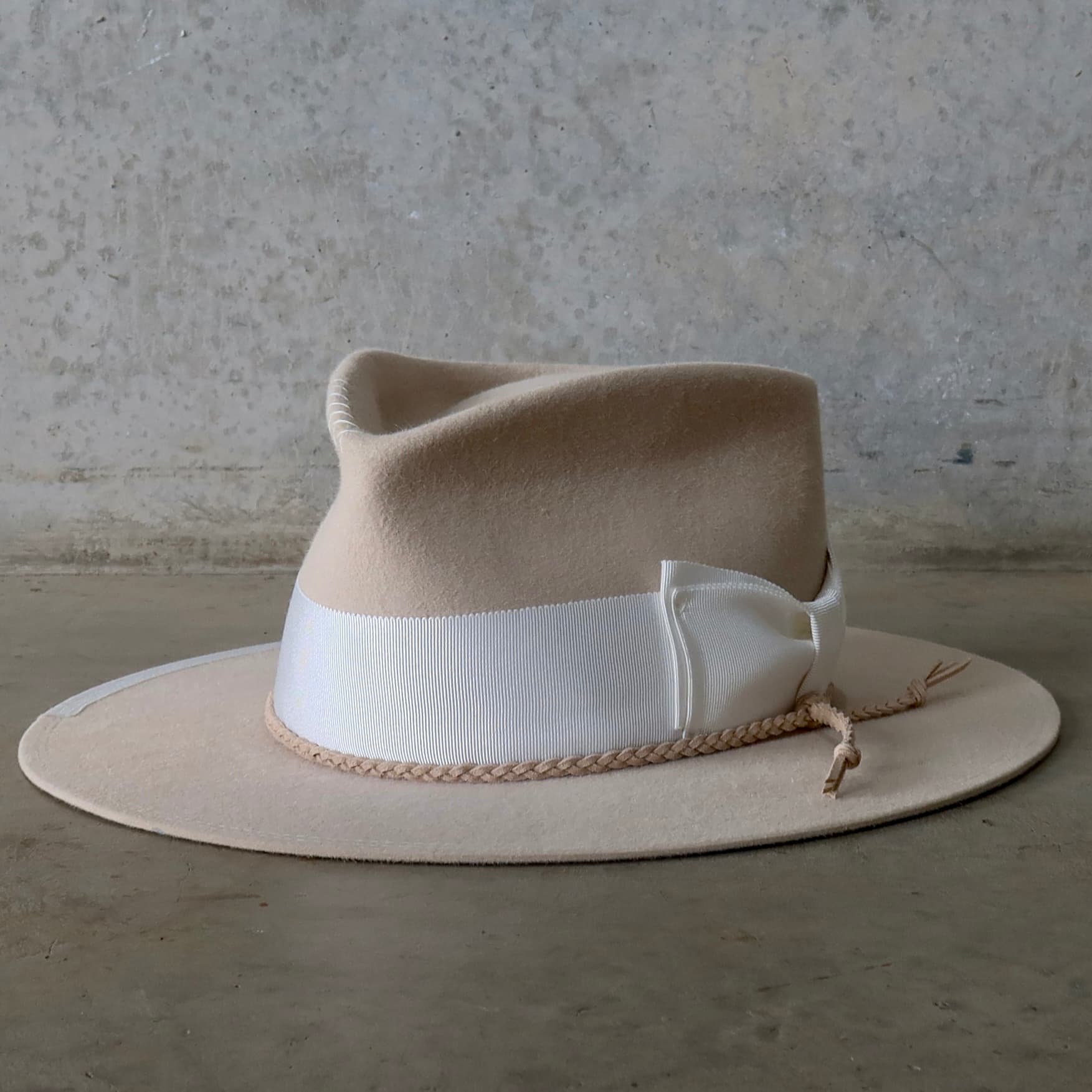 Front left angle of the beige felt hat Yolande by PHYLLi Designs with ivory grosgrain bow band and nude plaited suede string.
