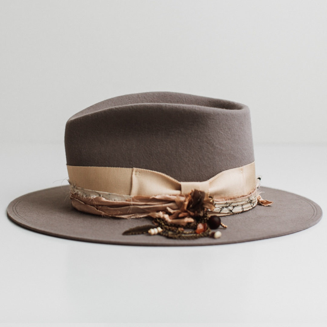 Left side view of the Arrowtown taupe felt hat by PHYLLi Designs with sand grosgrain band, bronze chunky hat pin and sari silk trimming.