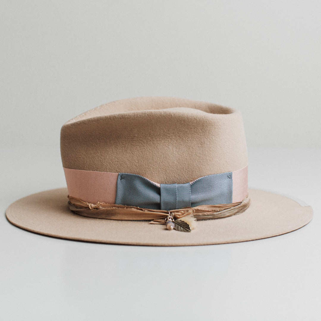 Left side view of the Eleanor beige felt hat by PHYLLi Designs with charm cluster featuring tassel, silver charm and beads.