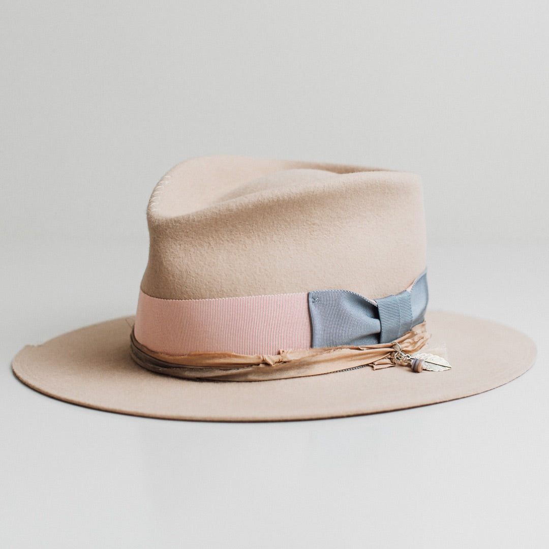 Front left angle of the Eleanor beige felt hat by PHYLLi Designs with cornflower grosgrain bow and peach and pale blue sari silk trimming.