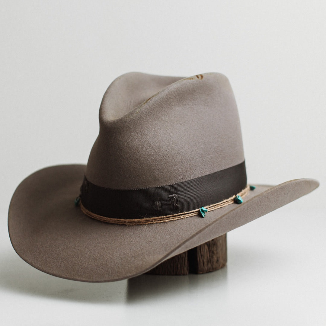 Front left angle of the Finse cement felt cowboy hat by PHYLLi Designs with distressed steel grey grosgrain band and turquoise beaded twine wraps.
